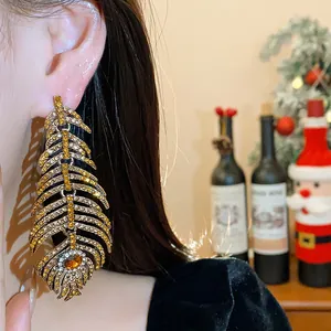 Close-up detail of large golden feather earrings with sparkling crystals worn on ear