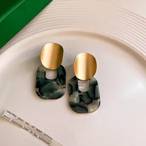 Macro view of vintage earrings with matte gold finish and green marbled resin drops