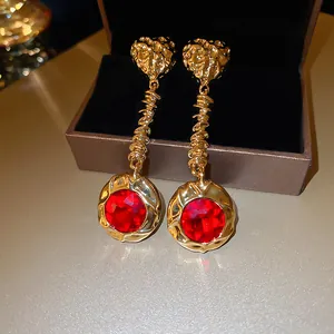 Close-up of elegant gold-toned drop earrings featuring large red faceted crystals