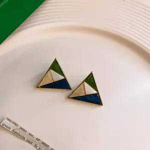 Close-up of geometric triangle stud earrings with green and blue enamel sections