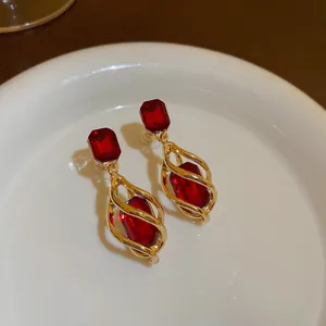 Close-up of elegant gold earrings with faceted red stones in a spiral cage design