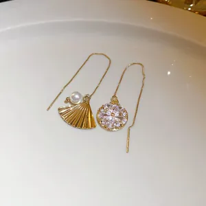 Detailed macro view of asymmetric gold threader earrings with fan, pearl, and crystal charms