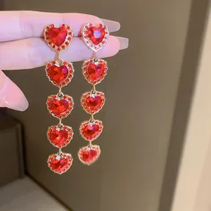 Detailed close-up of long dangling heart earrings with red rhinestones and gold plating