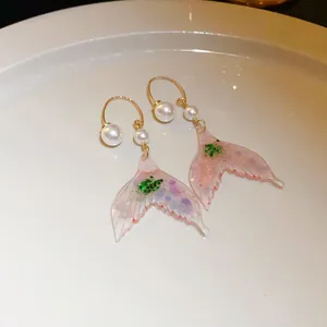 Elegant mermaid tail earrings featuring pearls and pink resin displayed on a white plate