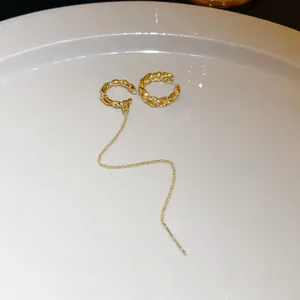 Detailed close-up of gold-plated textured ear cuff with long tassel chain earring on plate