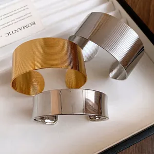 Elegant wide cuff bracelets in gold and silver with ribbed and smooth textures.