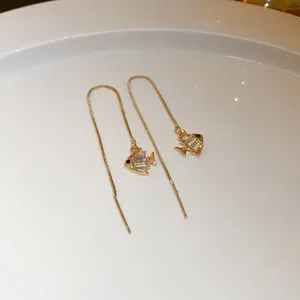 Detail view of gold threader earrings featuring a sparkling fish charm with crystals.