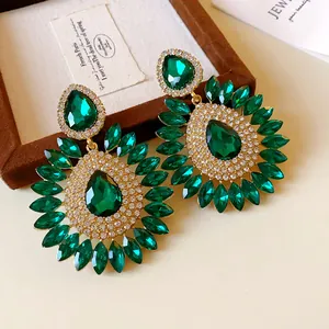 Detailed view of green teardrop emerald earrings with sparkling rhinestone floral design.