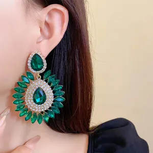 Close-up detail of luxury oversized green crystal flower teardrop earrings worn on ear