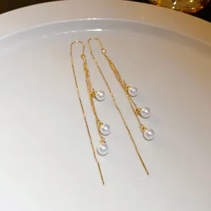 Elegant long gold tassel earrings featuring dangling white pearls on a white plate