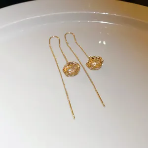 Macro view of gold threader earrings featuring a hollow cage ball with sparkling crystals.