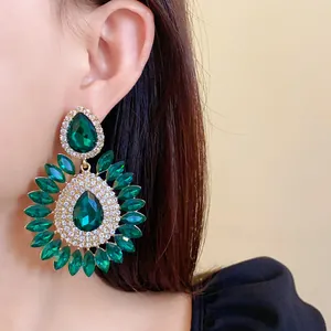 Elegant macro detail of exaggerated emerald green rhinestone drop floral earrings worn by a model