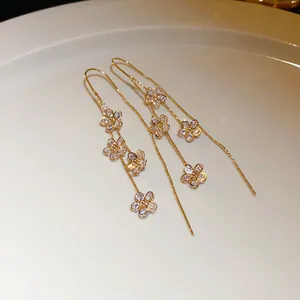 Detailed macro view of gold-toned threader earrings with zircon-encrusted flower charms.