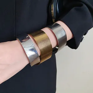 Detail shot of wide stainless steel textured and smooth open cuff bracelets in metallic tones