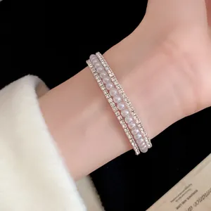 Primo piano di un elegante bracciale a tre file di perle e strass indossato al polso