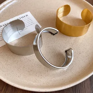 Close-up of gold and silver textured stainless steel wide open cuff bracelets on a plate