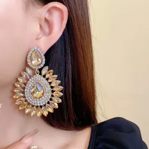 Detail view of exaggerated champagne crystal flower drop earrings worn by a model