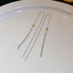 Detail view of long silver-colored threader earrings with star pendants on a white plate