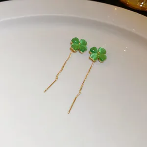 Close-up view of green cat-eye clover long tassel ear threader earrings on white plate
