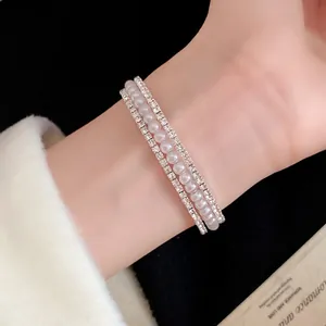 Dettaglio di un elegante bracciale rigido a tre strati con perle e strass sul polso.