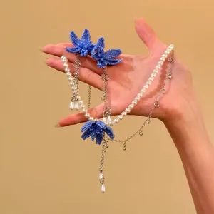 Elegant blue beaded flower and pearl jewelry set including necklace and earrings on hand