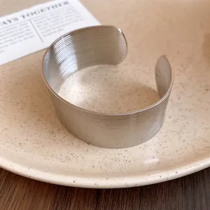 Close-up of a wide stainless steel open bangle with horizontal textured finish