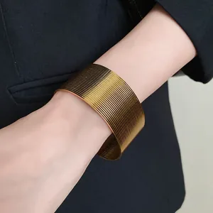 Detailed view of a wide textured gold cuff bracelet on a wrist against black fabric