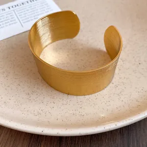 Macro view of a gold-finish wide open cuff bracelet with a horizontal ribbed texture.