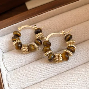 Elegante goldene Creolen mit künstlichen Tigerauge-Perlen in einer edlen Schmuckschatulle.