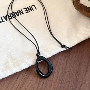 Close-up of a minimalist black irregular geometric pendant necklace on a cord.