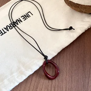 Detail of a dark red irregular oval pendant necklace on a minimalist canvas background