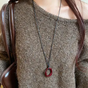 Detailed view of red resin geometric pendant on a long cord necklace with a vintage sweater