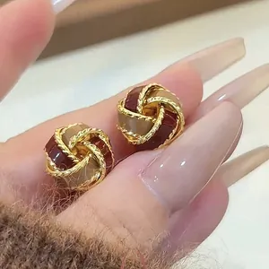 Close-up detail of retro Ancora red twisted knot stud earrings with gold trim