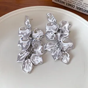 Primer plano de pendientes largos de flores de metal plateado con capas de pétalos