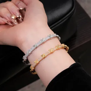 Gros plan de joncs en or et argent pavés de zircons avec motifs en X portés au poignet.