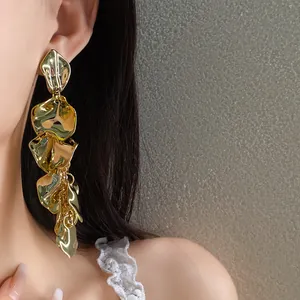 Primer plano de elegantes pendientes largos de metal dorado con forma de pétalo