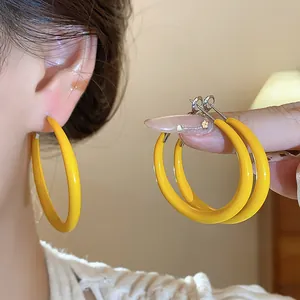 Close-up detail of stylish large yellow enamel hoop earrings featuring silver needles