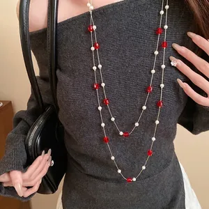 Elegant long layered pearl necklace with red faceted beads on a dark knit sweater