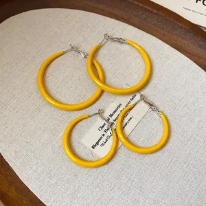 Close-up of bright yellow minimalist hoop earrings on a textured fabric background
