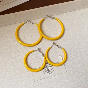 Top view of yellow enamel hoop earrings in two sizes on textured background