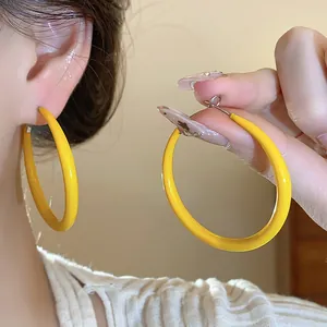 Macro detail showing minimalist bright yellow enamel hoop earrings with silver pins for women.