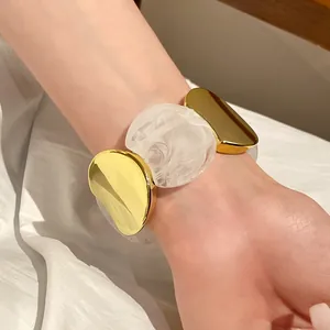 Primo piano del bracciale elastico in acrilico marmorizzato bianco e metallo dorato.