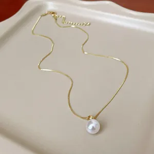 Dettaglio ravvicinato di una collana di perle dorate su un vassoio beige moderno.