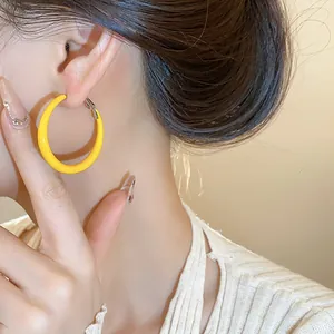 Close-up of vibrant yellow enamel hoop earrings worn by a model, sleek and modern.