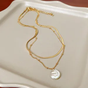 Dettaglio di una collana a due strati dorata con un elegante ciondolo di perla bianca tonda.