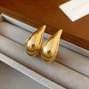 Close-up detail of elegant glossy gold water drop stud earrings in a grey jewelry tray