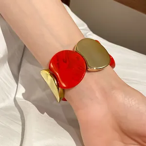 Primo piano di un grosso bracciale elastico in acrilico rosso e oro su un polso