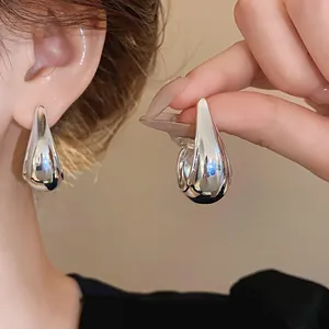 Close-up of minimalist silver needle teardrop earrings with a glossy metal finish.
