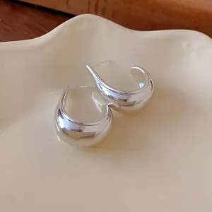 Detailed close-up of minimalist chunky silver water-drop earrings on a cream ceramic plate