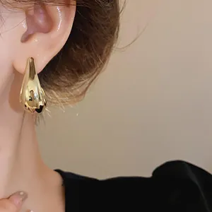 Close-up of elegant gold teardrop earrings worn on ear, showing polished metallic texture